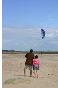 A man flying a small dual line power kite down at the beach.